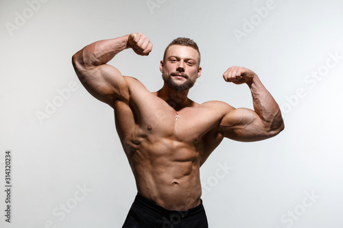 Foto Young muscular bodybuilder guy demonstrates his muscles isolated on a light gray background