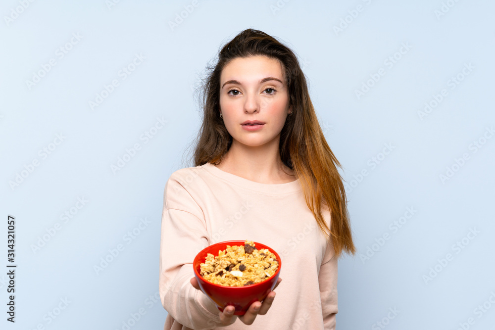 Young brunette girl over isolated blue background holding a bowl of cereals