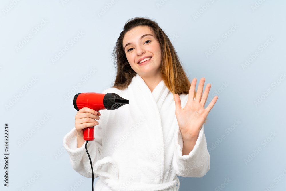 Young woman in a bathrobe with hair hairdryer saluting with hand with happy expression Young woman in a bathrobe with hair hairdryer saluting with hand with happy expression