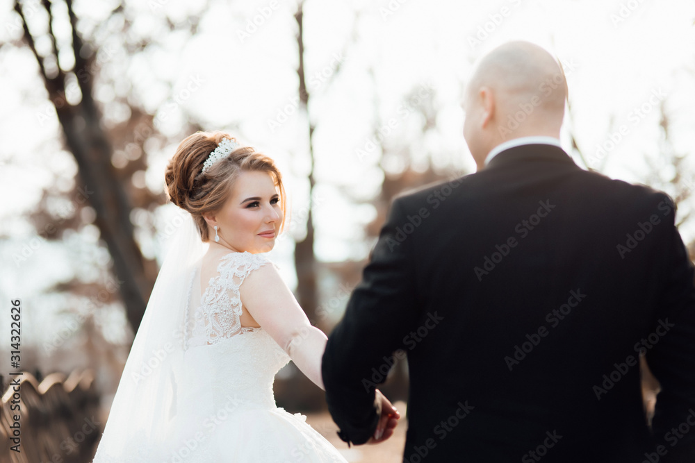 Stylish couple in love - the bride and groom - on a walk in their wedding day in a park, gently hugging and smiling. Newlyweds in autumn park. Stylish couple in love - the bride and groom - on a walk in their wedding day in a park, gently hugging and smiling. Newlyweds in autumn park.