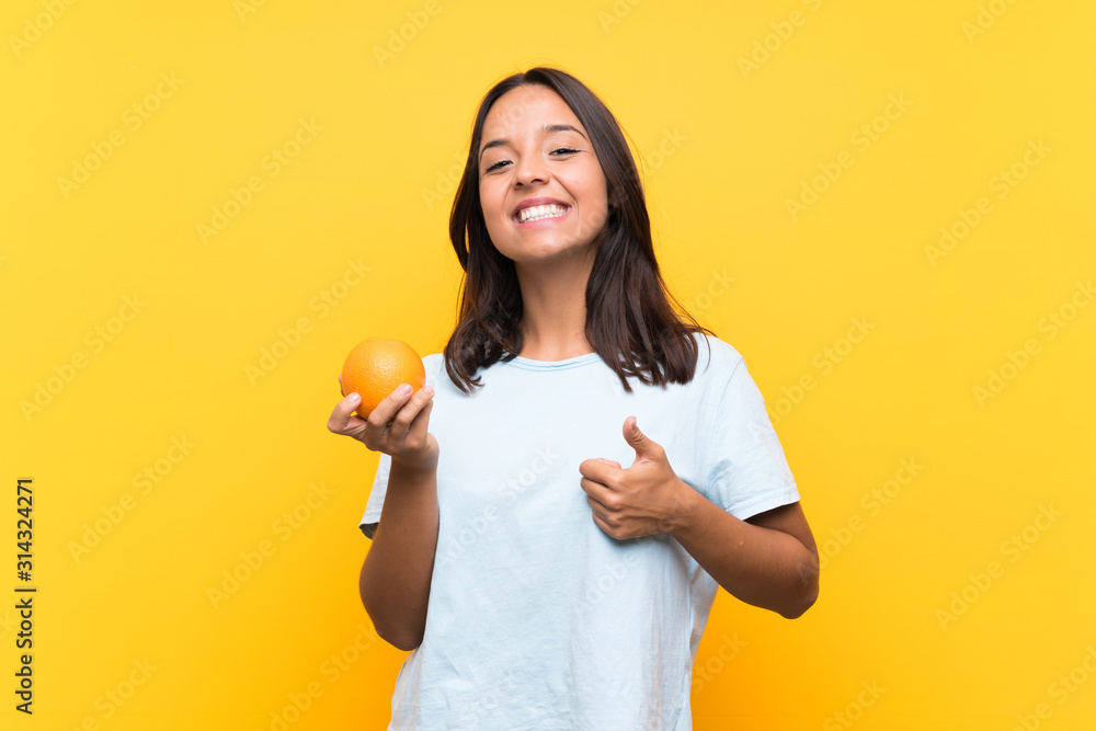 Young brunette woman holding an orange with thumbs up because something good has happened Young brunette woman holding an orange with thumbs up because something good has happened