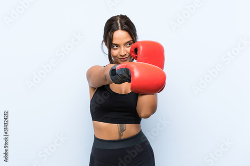Young sport girl with boxing gloves over isolated blue background © luismolinero