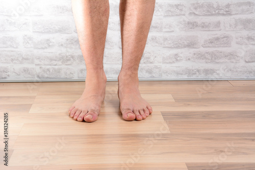 A man's naked legs standing at floor in the house.