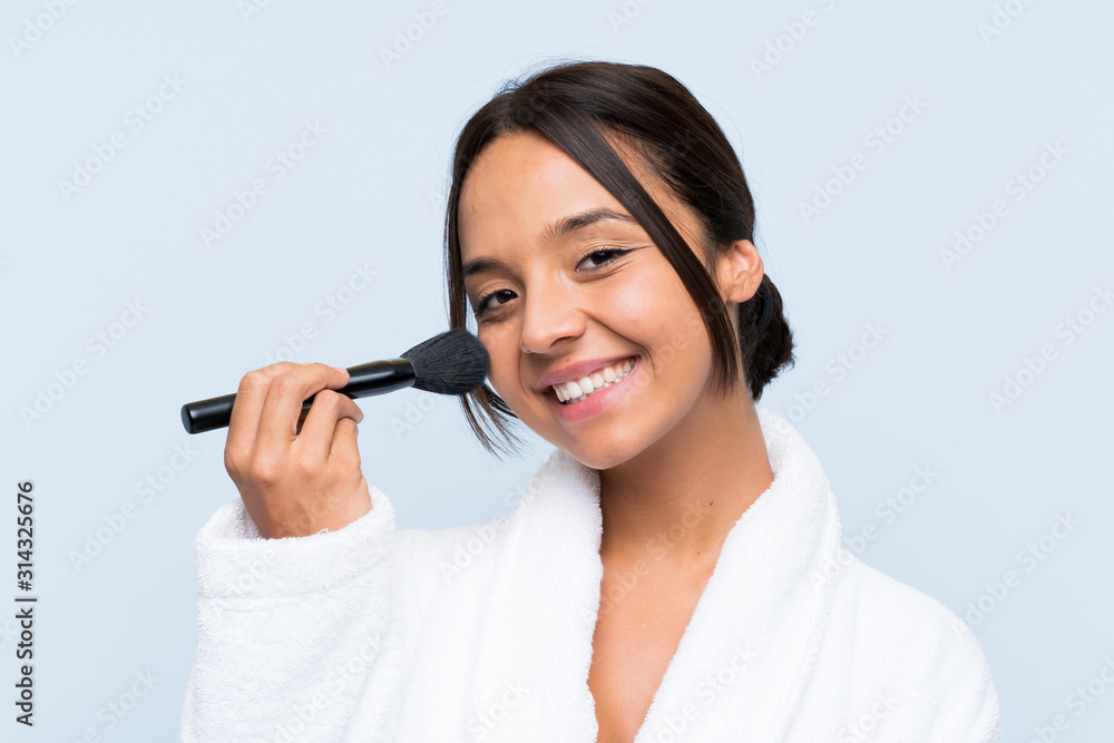 Young brunette girl in bathrobe with makeup over isolated blue background Young brunette girl in bathrobe with makeup over isolated blue background