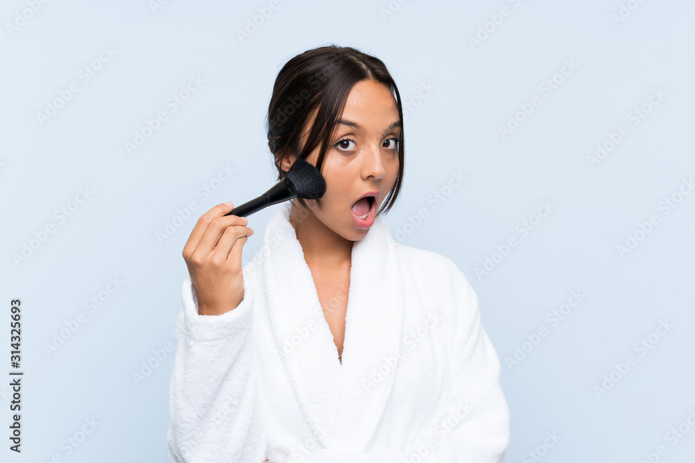 Young brunette girl in bathrobe with makeup over isolated blue background Young brunette girl in bathrobe with makeup over isolated blue background