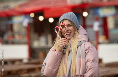 Portrait of a young beautiful happy woman with candy posing on the street of a European city. Xmas.