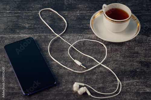 Headphones in the form of a treble clef symbol. on a wooden background with a Cup of tea and a smartphone