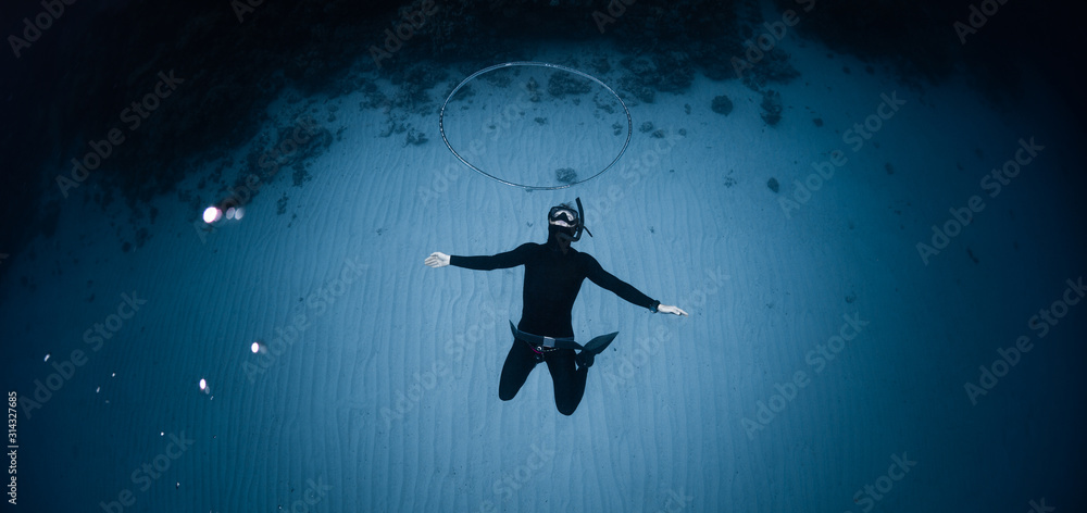 Freediver hangs deep underwater over the sandy bottom and blows the huge ring bubble