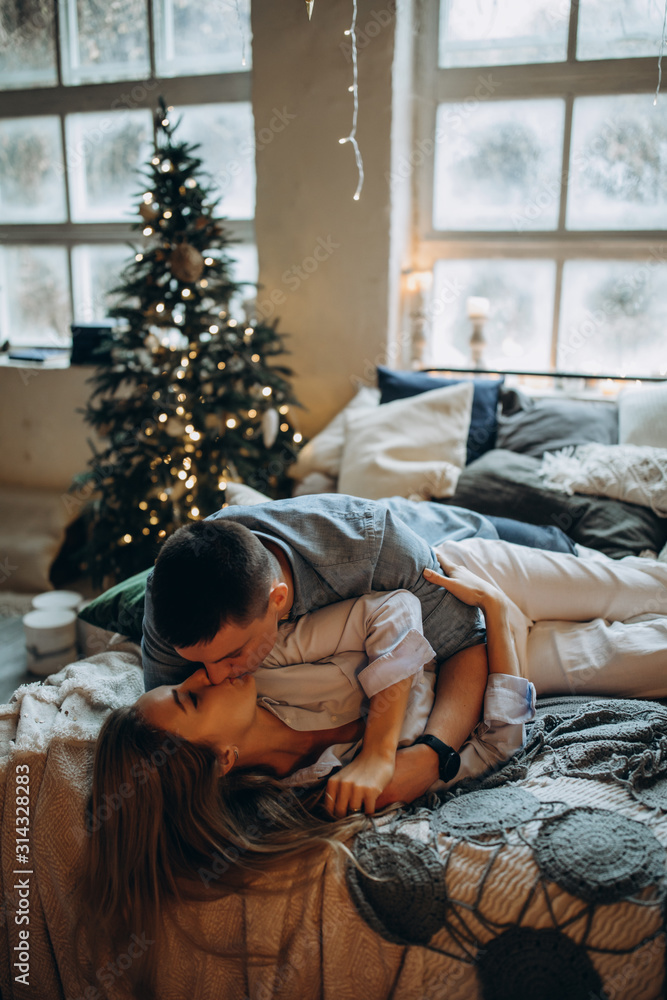 Obraz premium A guy with a girl is celebrating Christmas. A loving couple enjoys each other on New Year's Eve in a cozy home environment. New Year's love story.