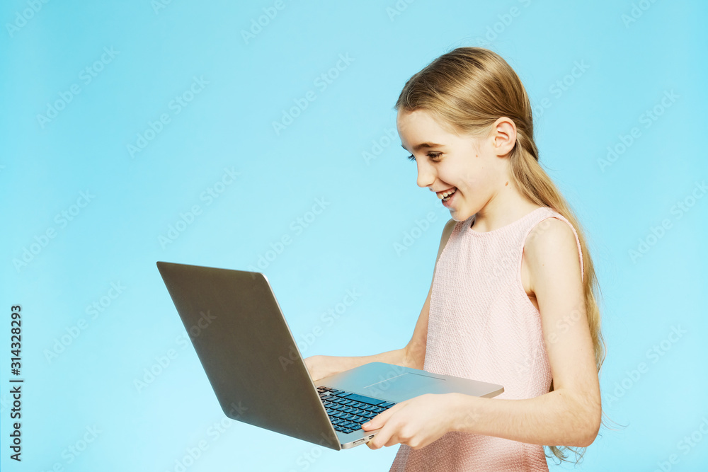 Isolated girl is having fun looking at the computer on a blue background. The concept of emotions. Girl with a computer. Isolated girl is having fun looking at the computer on a blue background. The concept of emotions. Girl with a computer.