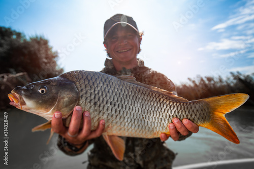 Happy fisherman holds the big Carp fish (Cyprinus carpio) and smiles