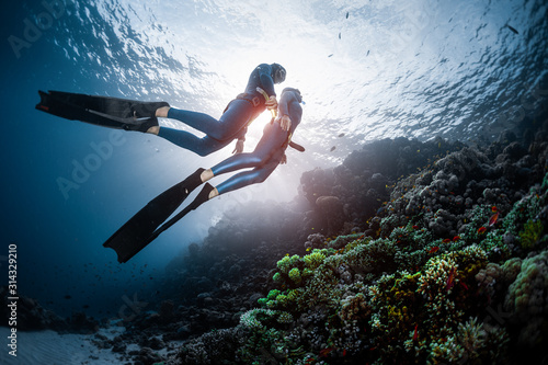 Two freedivers swim over the vivid coral reef in a tropical sea during their recreational freedive session