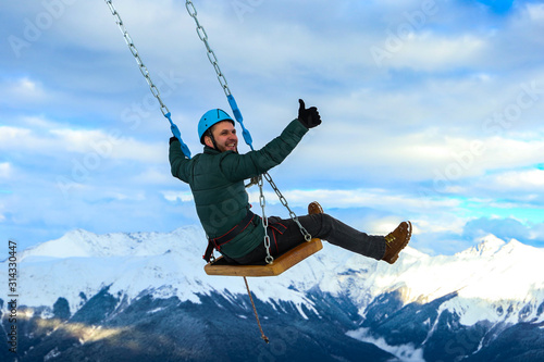 A young athletic man swings on a swing over a precipice on snow covered mountain peaks