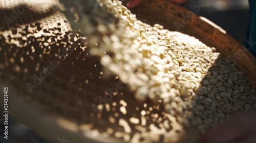 Thai male hand with wooden spoon roasting Arabica coffee beans in a clay pan. The traditional process of fry coffee beans  in Thailand