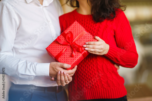 Red gift box in the hands of a couple in love. Valentine's Day, holiday and surprise concept. Lovers give each other presents. Relationship and love concept. © maxbelchenko