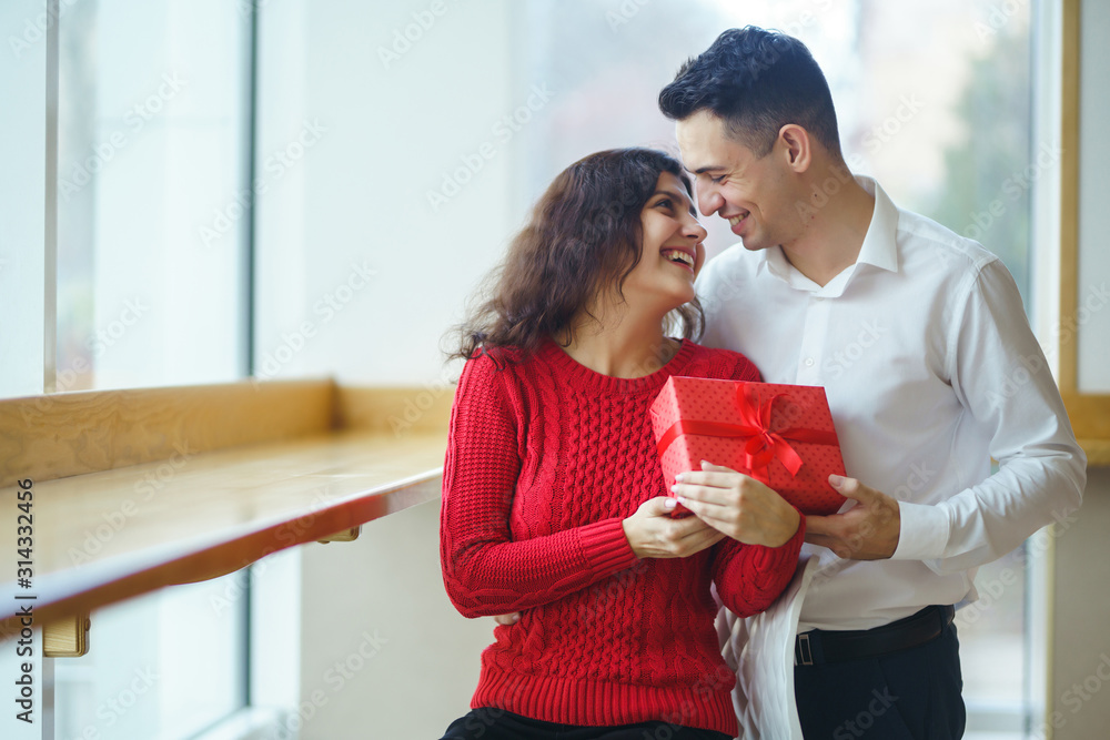Happy couple with gift hugging. Red gift box in the hands of a couple in love. Valentine's Day, holiday and surprise concept. Lovers give each other presents. Relationship and love concept. Happy couple with gift hugging. Red gift box in the hands of a couple in love. Valentine's Day, holiday and surprise concept. Lovers give each other presents. Relationship and love concept.