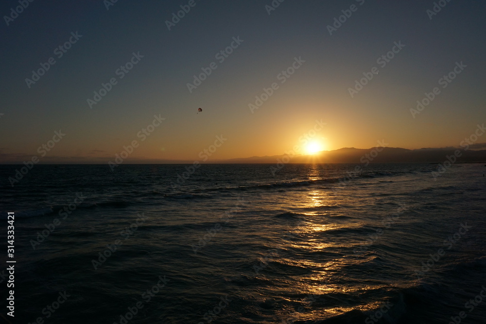 Sun going down behind a surfer and Paraglider off the beaches of Santa Monica, California Sun going down behind a surfer and Paraglider off the beaches of Santa Monica, California