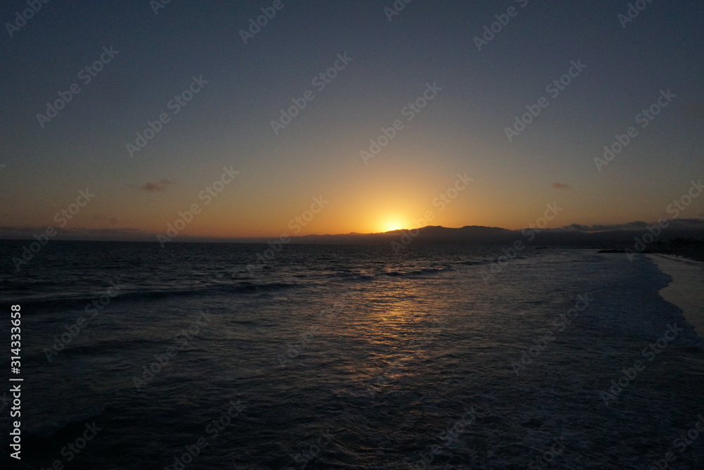 Sunsetting behind the mountains just off the beach of Santa Monica, California with a surfer and paraglider enjoying the views Sunsetting behind the mountains just off the beach of Santa Monica, California with a surfer and paraglider enjoying the views