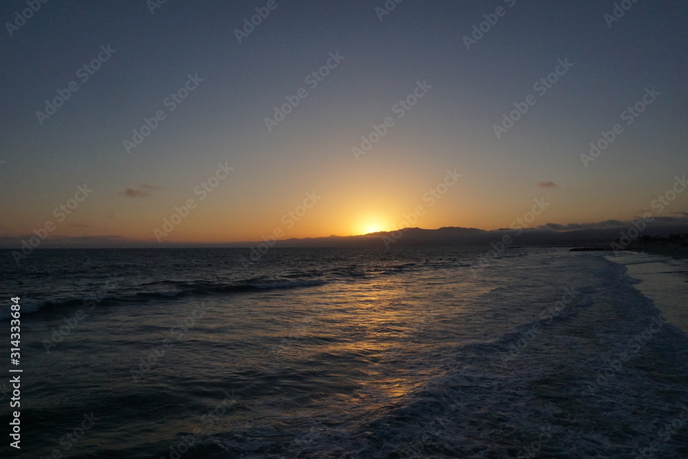 Sunsetting behind the mountains just off the beach of Santa Monica, California with a surfer and paraglider enjoying the views Sunsetting behind the mountains just off the beach of Santa Monica, California with a surfer and paraglider enjoying the views