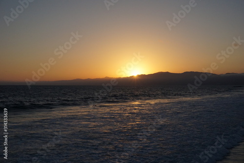 Sunsetting behind the mountains just off the beach of Santa Monica, California with a surfer and paraglider enjoying the views