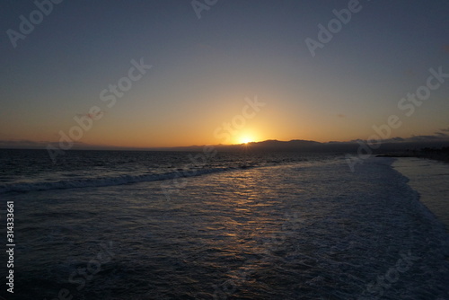 Sunsetting behind the mountains just off the beach of Santa Monica, California with a surfer and paraglider enjoying the views