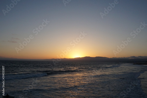 Sunsetting behind the mountains just off the beach of Santa Monica  California with a surfer and paraglider enjoying the views