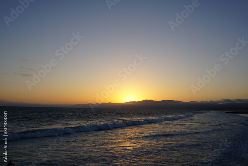 Sunsetting behind the mountains just off the beach of Santa Monica  California with a surfer and paraglider enjoying the views