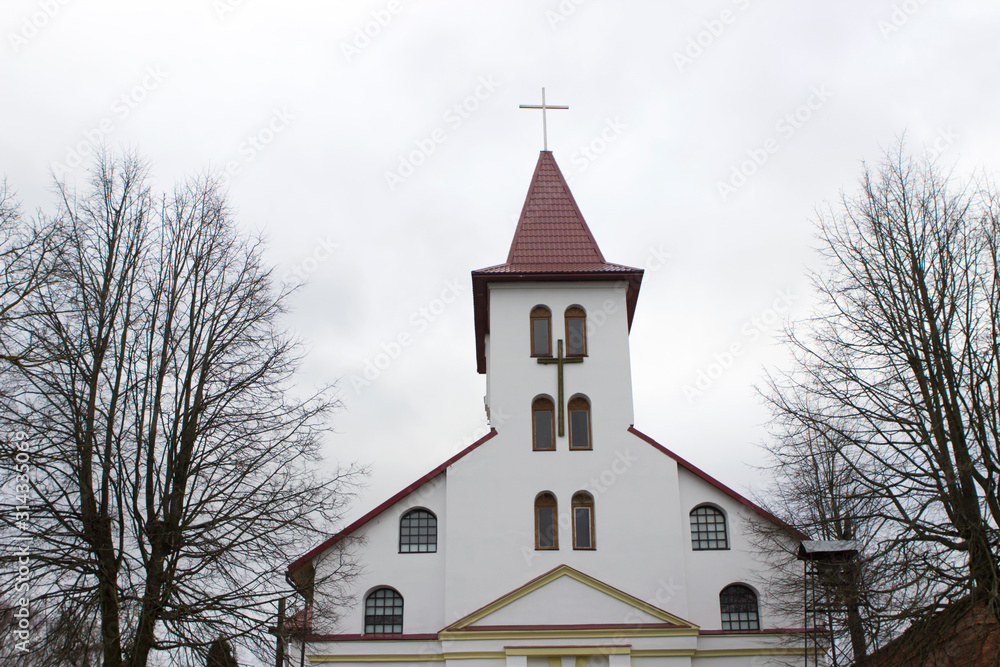 A small local catholic white church with a red roof. Tree branches.