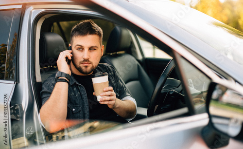 Young handsome driver man with smartphone serfing internet and drink black coffee