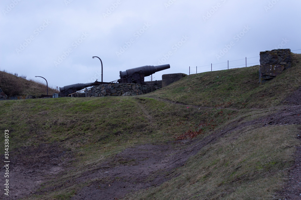 Fototapeta premium Old cast-iron artillery Russian cannon, old granite fortifications of the island-fort Suomenlinna overgrown with grass, Suomenlinna, gloomy autumn day in Finland.