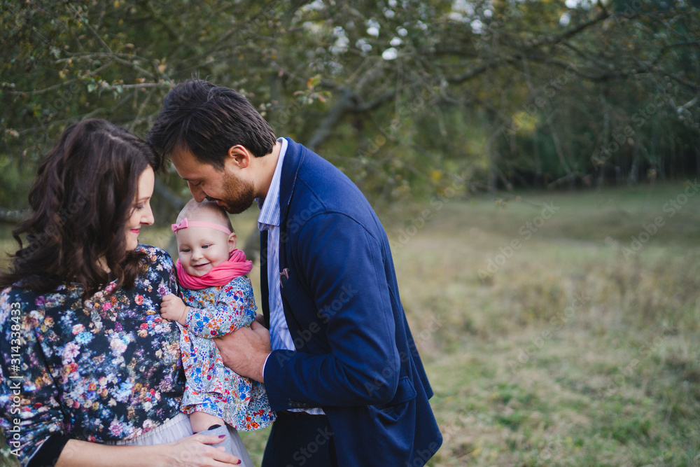 Fototapeta premium Young happy caucasian couple with little baby girl. Parents and daughter walking and having fun together. Mother and father play with child outdoors. Family, parenthood, childhood, happiness concept.