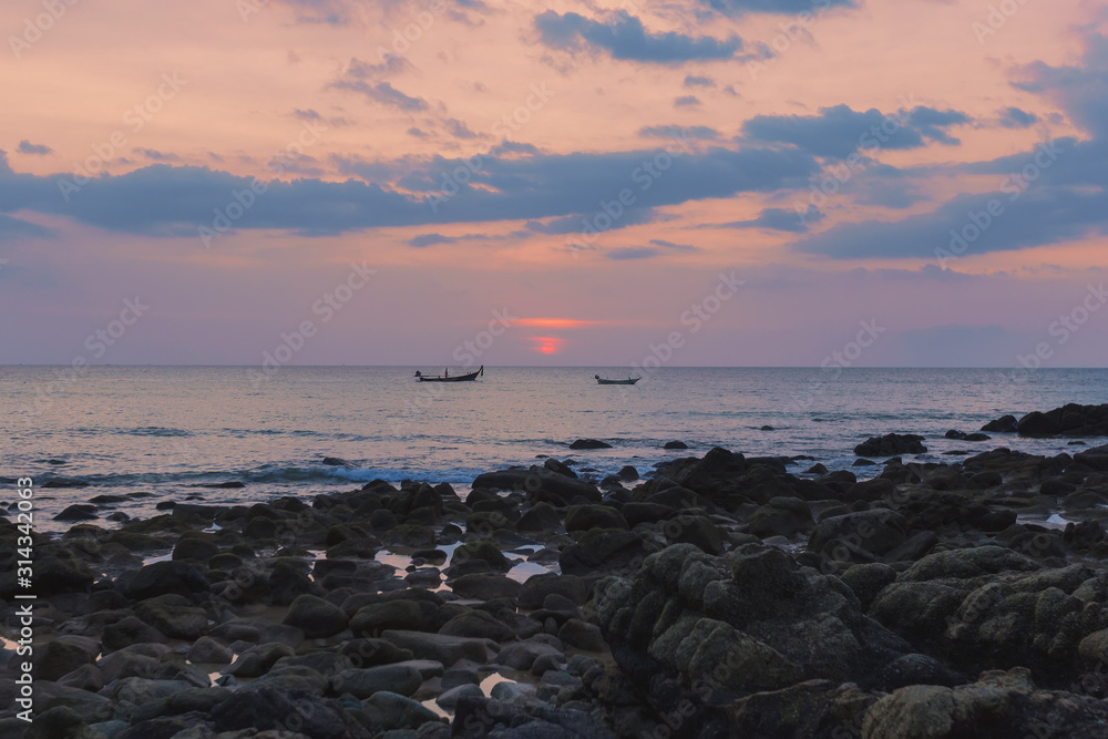 Colorful Thai red sunset, blue clouds calm sea, 2 fisherman boats on the horizon, stone beach