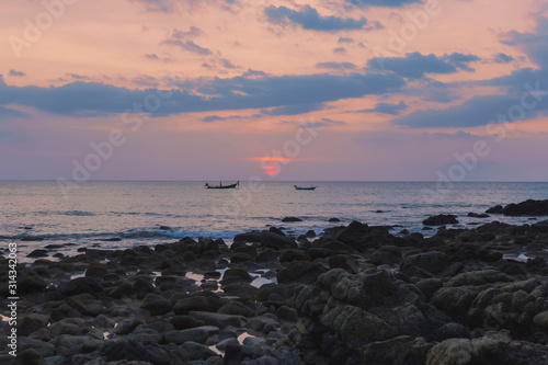 Colorful Thai red sunset, blue clouds calm sea, 2 fisherman boats on the horizon, stone beach © Olha