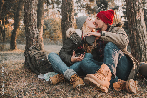 Travel couple camping with thermos in the forest. Concept of trekking, adventure and seasonal vacation.