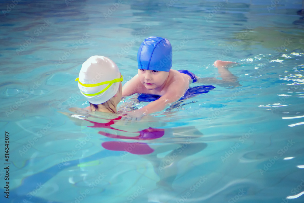 Little boy using the kickboard for learning to swim with trainer in the swimming pool
