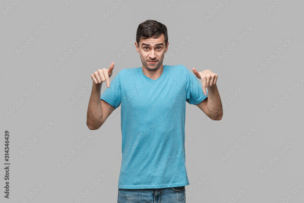 Pretty man in a blue tee pointing with a finger at the copy space isolater over grey background. Pretty man in a blue tee pointing with a finger at the copy space isolater over grey background.