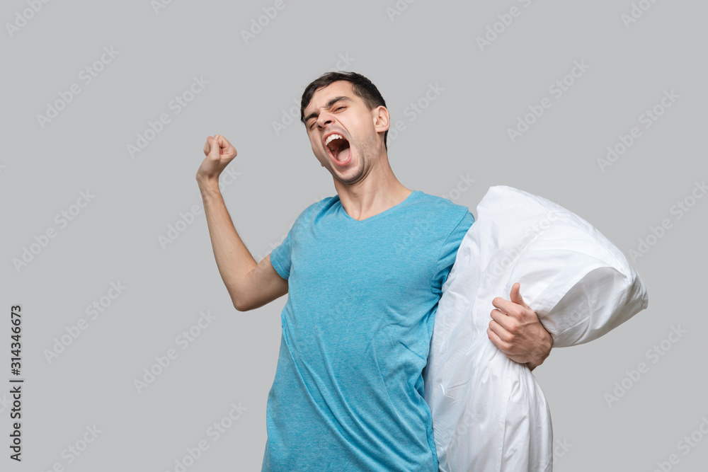 Tired brunet man in a blue tee resting on a white pillow isolated over grey background. Tired brunet man in a blue tee resting on a white pillow isolated over grey background.
