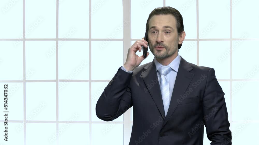 Confident mature businessman talking on mobile phone. Serious male executive on checkered window background. Confident mature businessman talking on mobile phone. Serious male executive on checkered window background.
