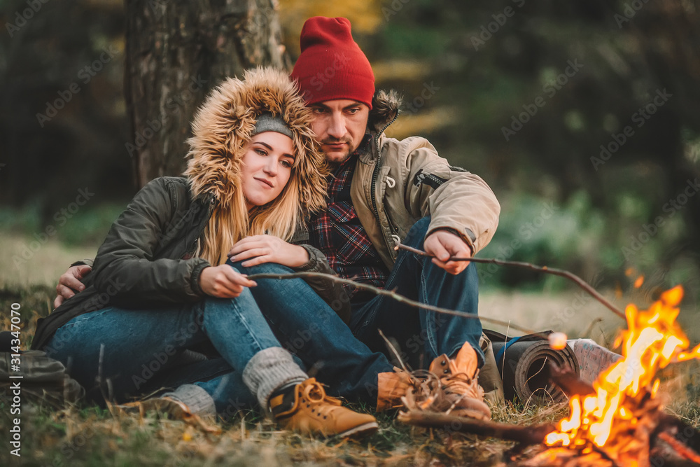 Traveler couple camping and roasting marshmallows over the fire in the forest after a hard day. Concept of trekking, adventure and seasonal vacation. Traveler couple camping and roasting marshmallows over the fire in the forest after a hard day. Concept of trekking, adventure and seasonal vacation.