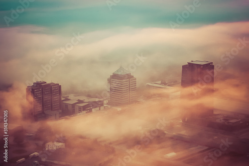 Aerial view of a foggy sunrise over a residential and industrial area of a city. Fog layered over houses below early morning sunrise.