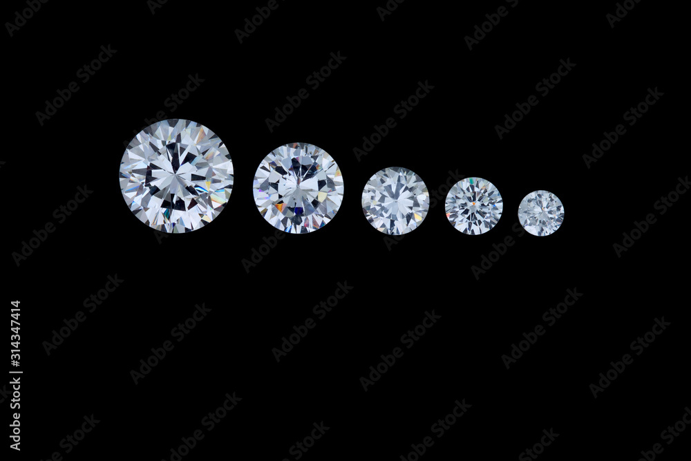 A row of five round faceted diamonds going from smallest to largest sits on a black background. A row of five round faceted diamonds going from smallest to largest sits on a black background.