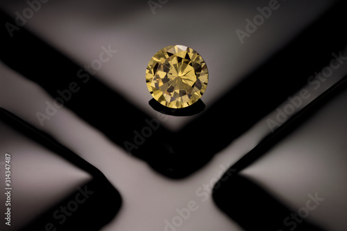 A solitaire, faceted, round yellow diamond sits on a reflective background of black of fuse glass squares.