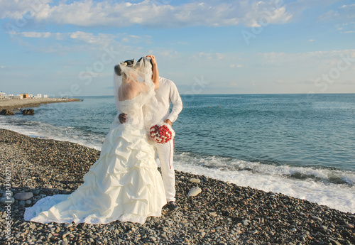 Wedding by the sea. Beautiful couple of newlyweds. Bride with a red bouquet in a wedding dress at the water.