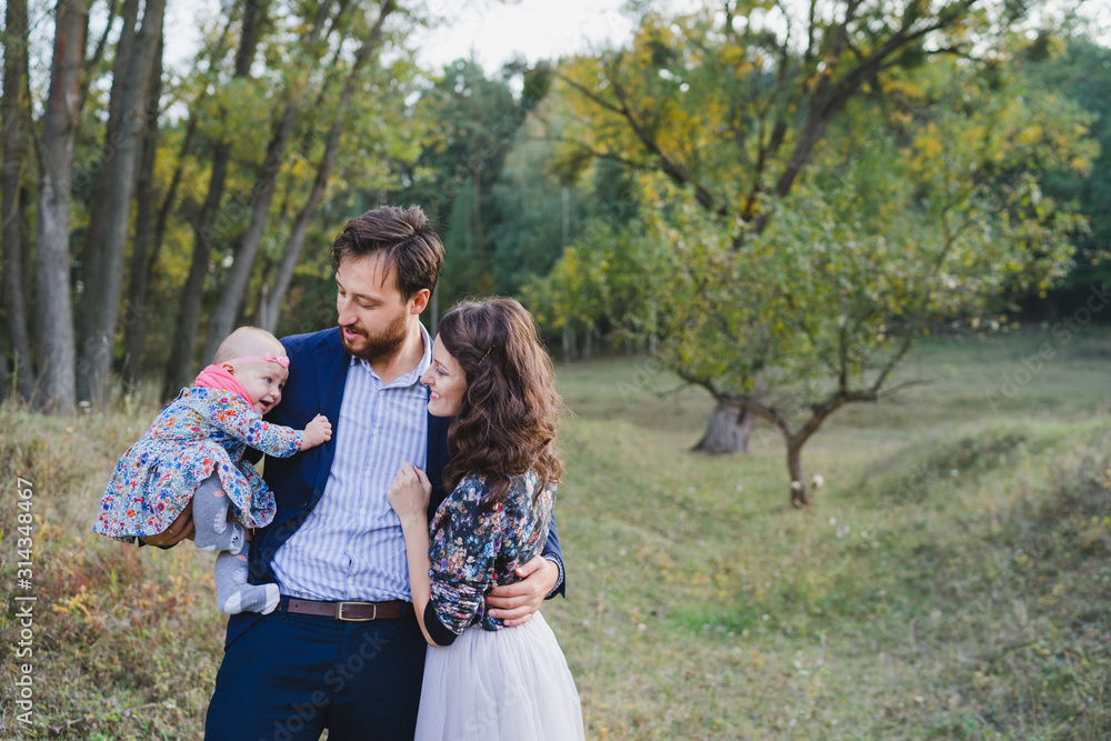 Fototapeta premium Young happy caucasian couple with little baby girl. Parents and daughter walking and having fun together. Mother and father play with child outdoors. Family, parenthood, childhood, happiness concept.