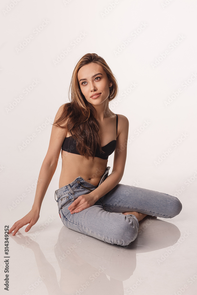 portrait of sexy smiling asian woman with long hair posing in black lingerie, blue jeans on white studio background. model tests of skinny girl in bra. attractive female sits on floor and smiles portrait of sexy smiling asian woman with long hair posing in black lingerie, blue jeans on white studio background. model tests of skinny girl in bra. attractive female sits on floor and smiles