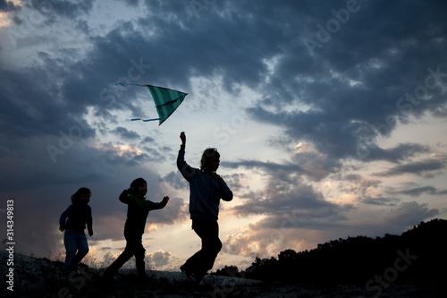 Children run with kite on summer sunset meadow silhouetted. playing outdoors.