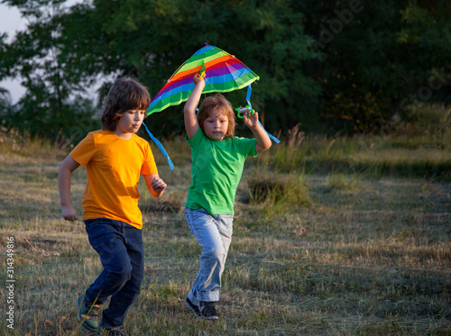 Children run with kite on summer sunset meadow. playing outdoors