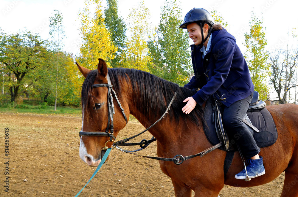 Happy and smiley young woman riding a brown horse. Autumn landscape in the background. Happy and smiley young woman riding a brown horse. Autumn landscape in the background.