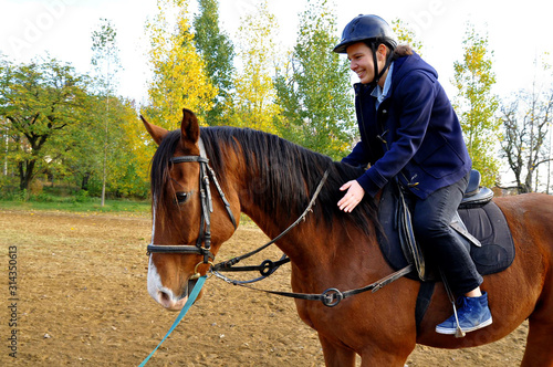 Happy and smiley young woman riding a brown horse. Autumn landscape in the background.