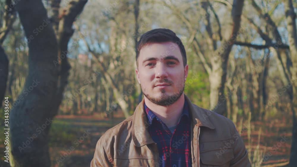 Young man on a background of trees without foliage. A guy in a leather jacket takes off his baseball cap and puts it on Santa hat or New Year's red cap. Young man on a background of trees without foliage. A guy in a leather jacket takes off his baseball cap and puts it on Santa hat or New Year's red cap.